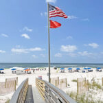 boardwalk to beach with American flag and red flag on flagpole