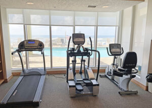 treadmill elliptical and exercise bike in workout room overlooking pool