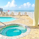 outdoor pool and hot tub with stone paver patio overlooking the white sand beach and gulf of Mexico